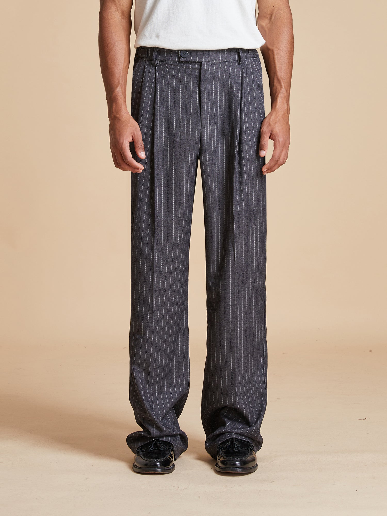 A man wearing Found Pinstripe Pleated Trousers and a white t-shirt.