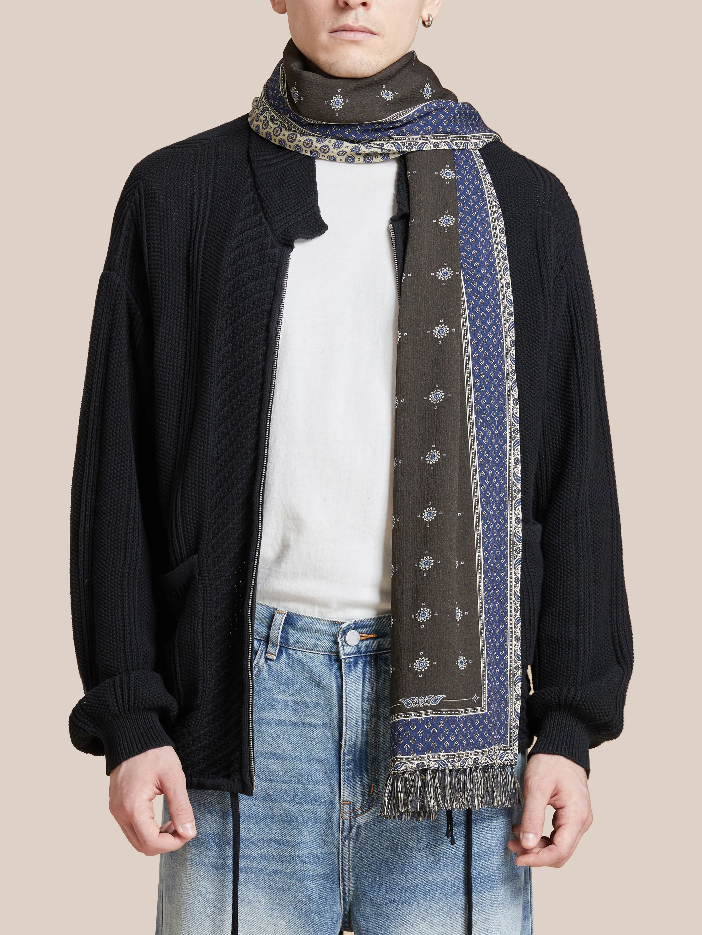 A person wears a black cardigan, white t-shirt, and blue jeans, complemented by the Found Black Royal Blue Print Scarf with Indo-Aryan prints.