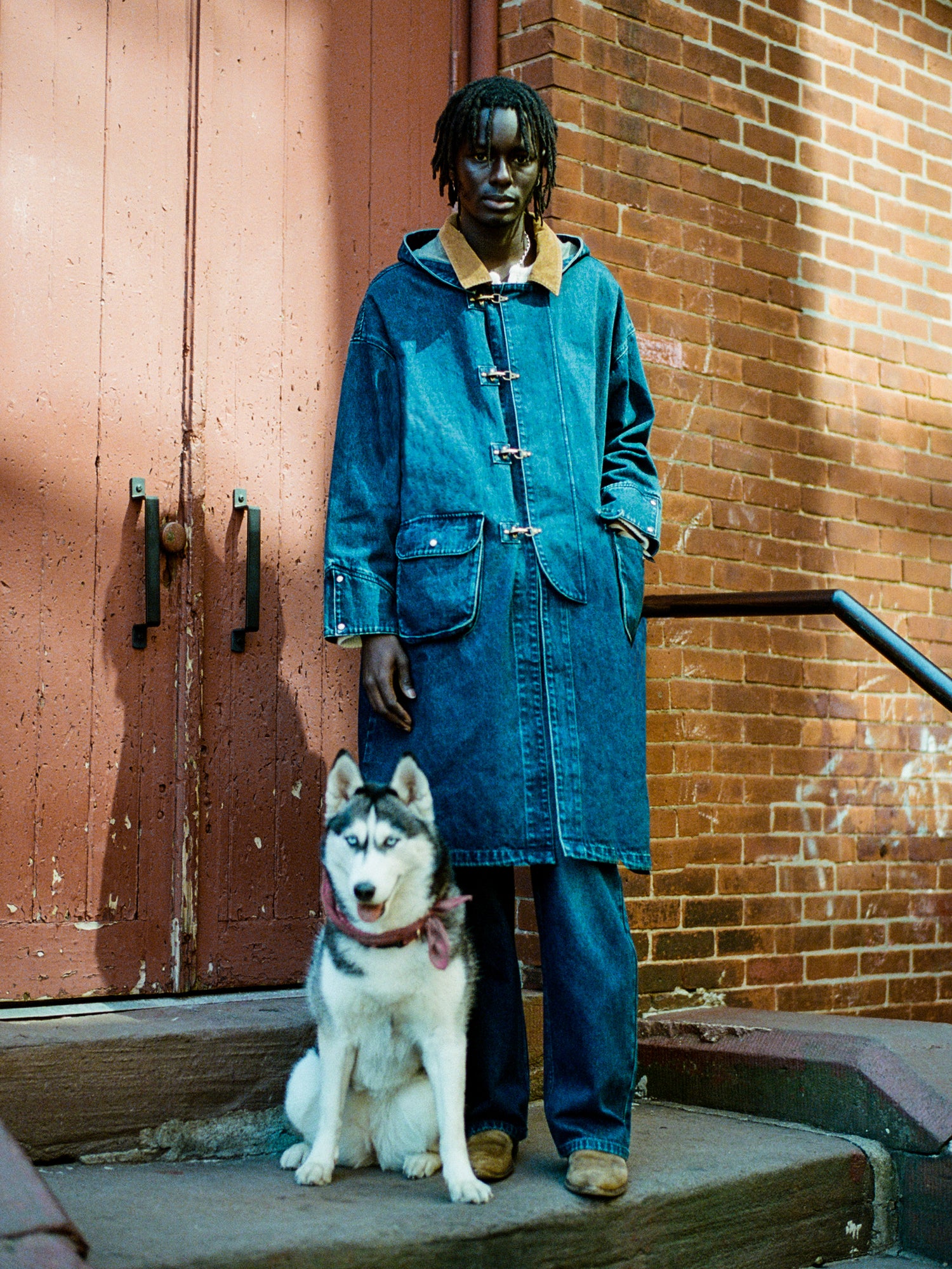 A man in a Sargasso Denim Buckle Coat by Found, standing next to a husky dog.