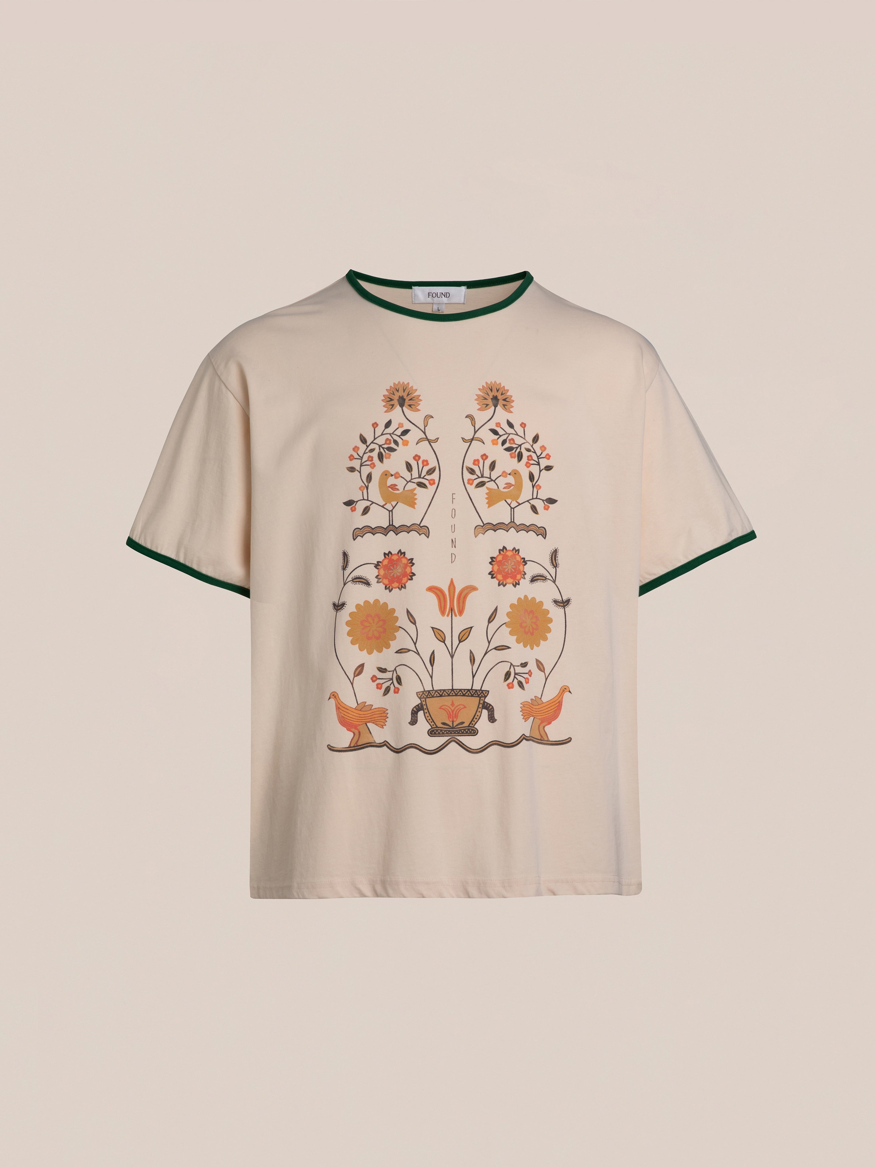 The Cascade Floral Ringer Tee by FOUND is a light beige, short-sleeve T-shirt adorned with an intricate floral and bird design in orange, yellow, and brown hues inspired by South Asian motifs. Dark green trim on the collar and sleeves adds to its classic ringer tee appeal.