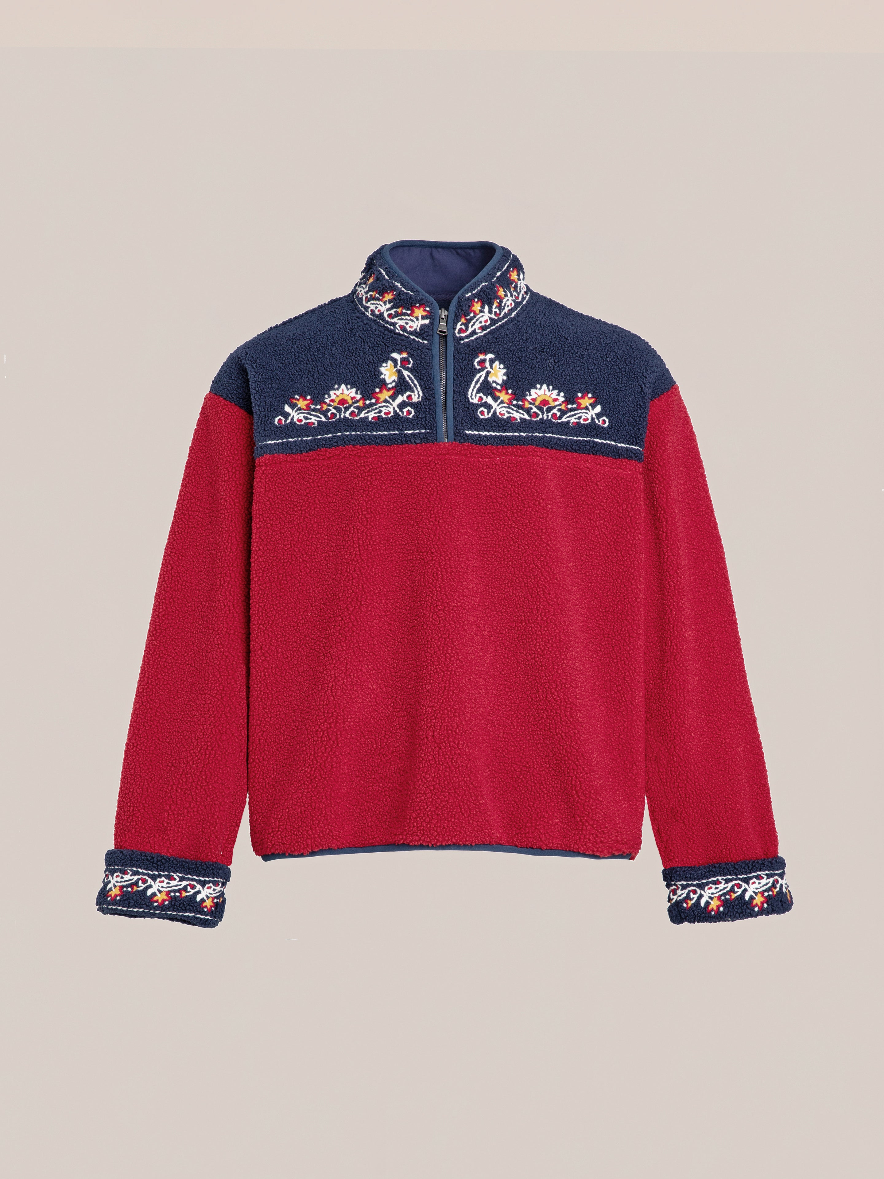 The FOUND Pahari Floral Embroidered Sherpa Pullover is a long-sleeve fleece garment with a red body and navy blue yoke, showcasing intricate Pahari style embroidery on the chest and cuffs.