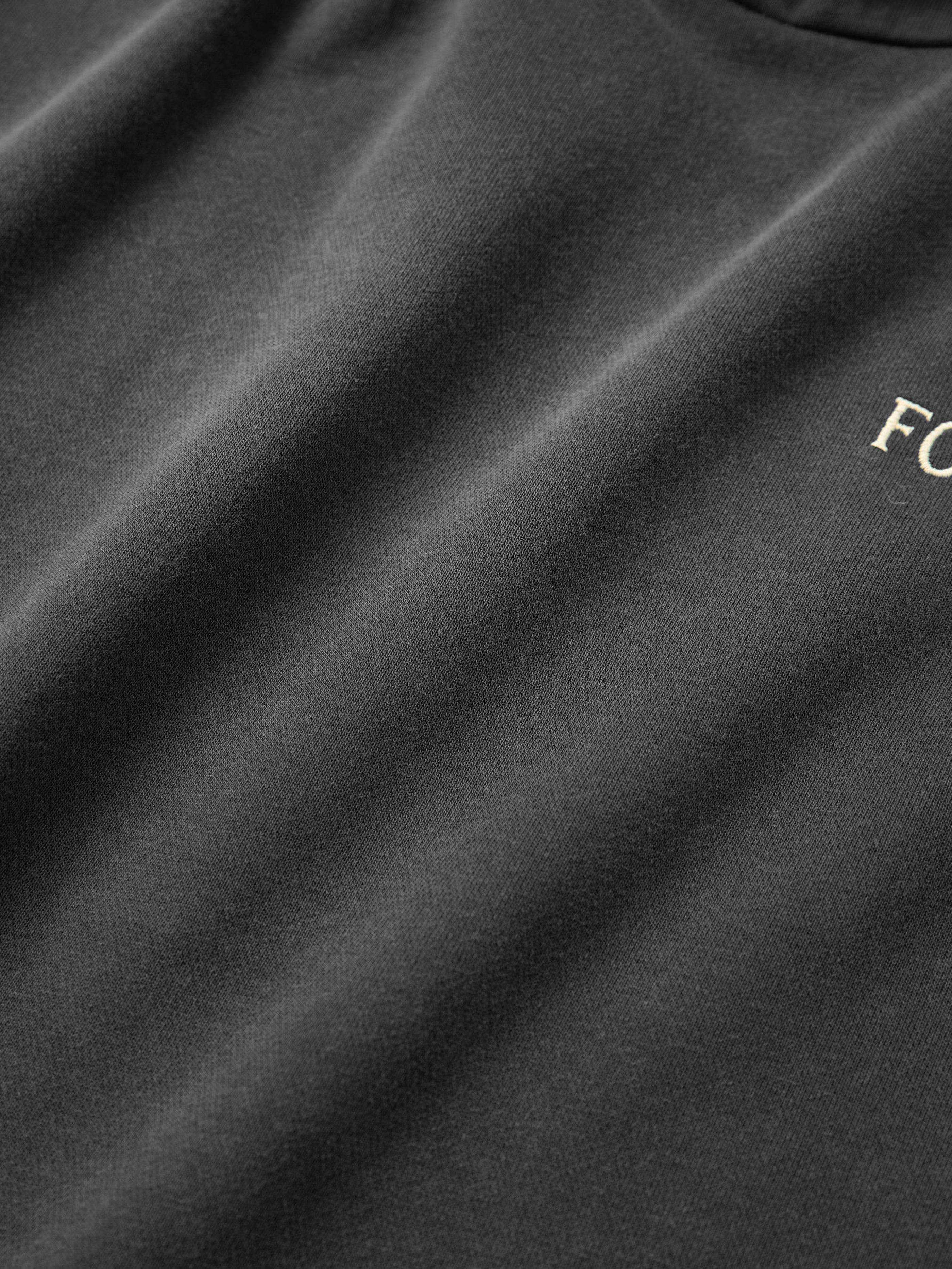 Close-up of a Stitched Border Distressed Logo Hoodie by FOUND, highlighting its vintage black design with partial white "F" and "C" letters, crafted from soft French Terry Cotton.