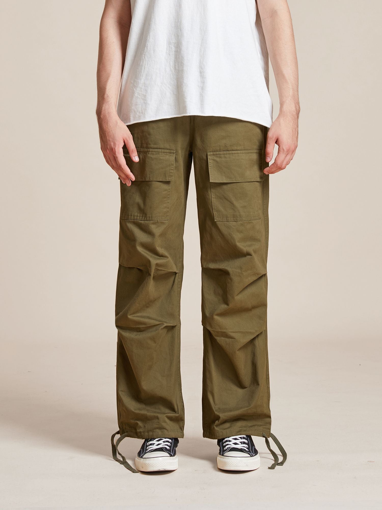 A person wearing olive green Parachute Cargo Twill Pants by Found and black and white sneakers stands with arms at their sides, displayed from the shoulders down against a plain background.