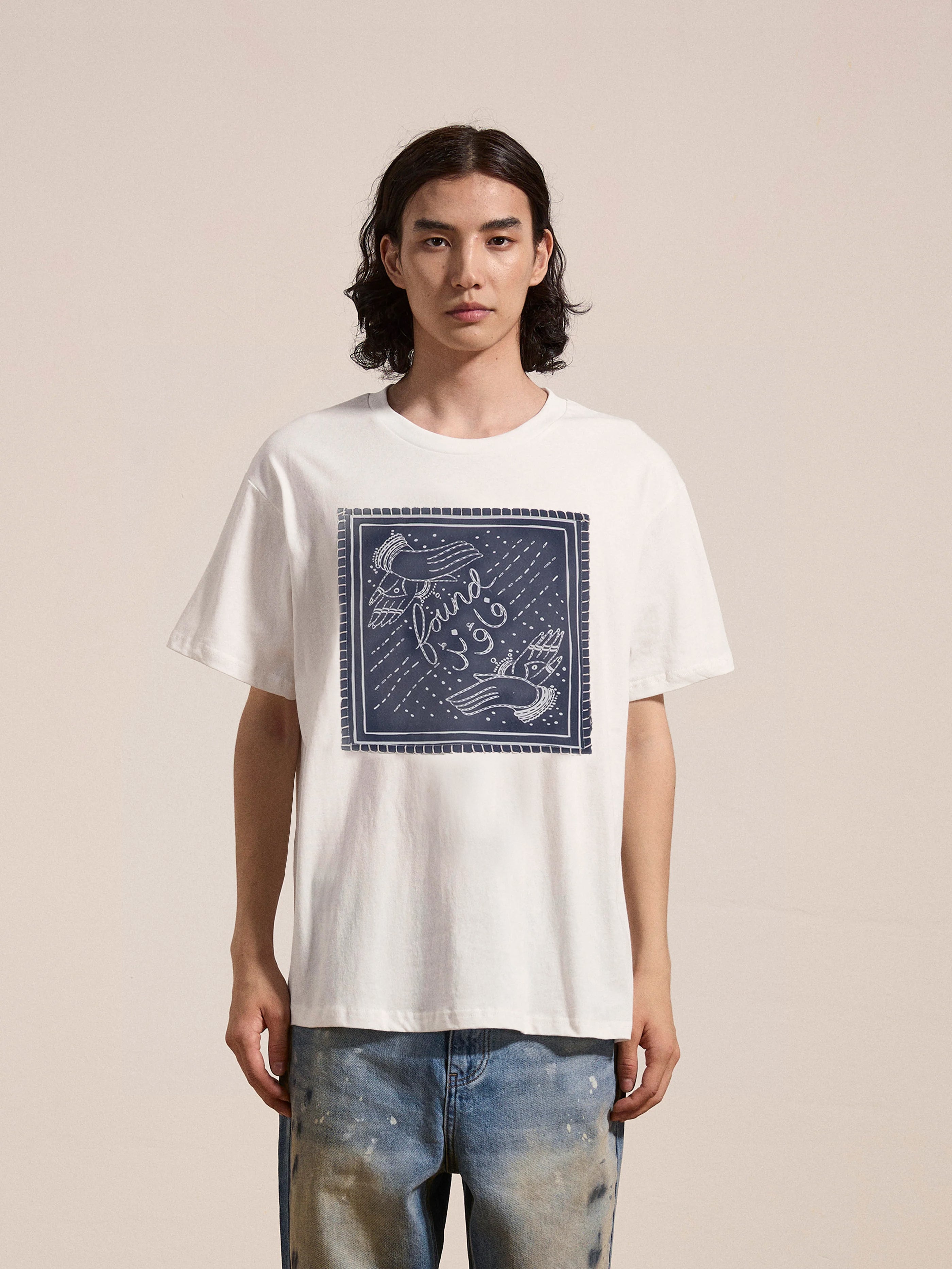 Person wearing a FOUND Hand Art Graphic Tee featuring a blue print, paired with faded jeans, against a plain background.