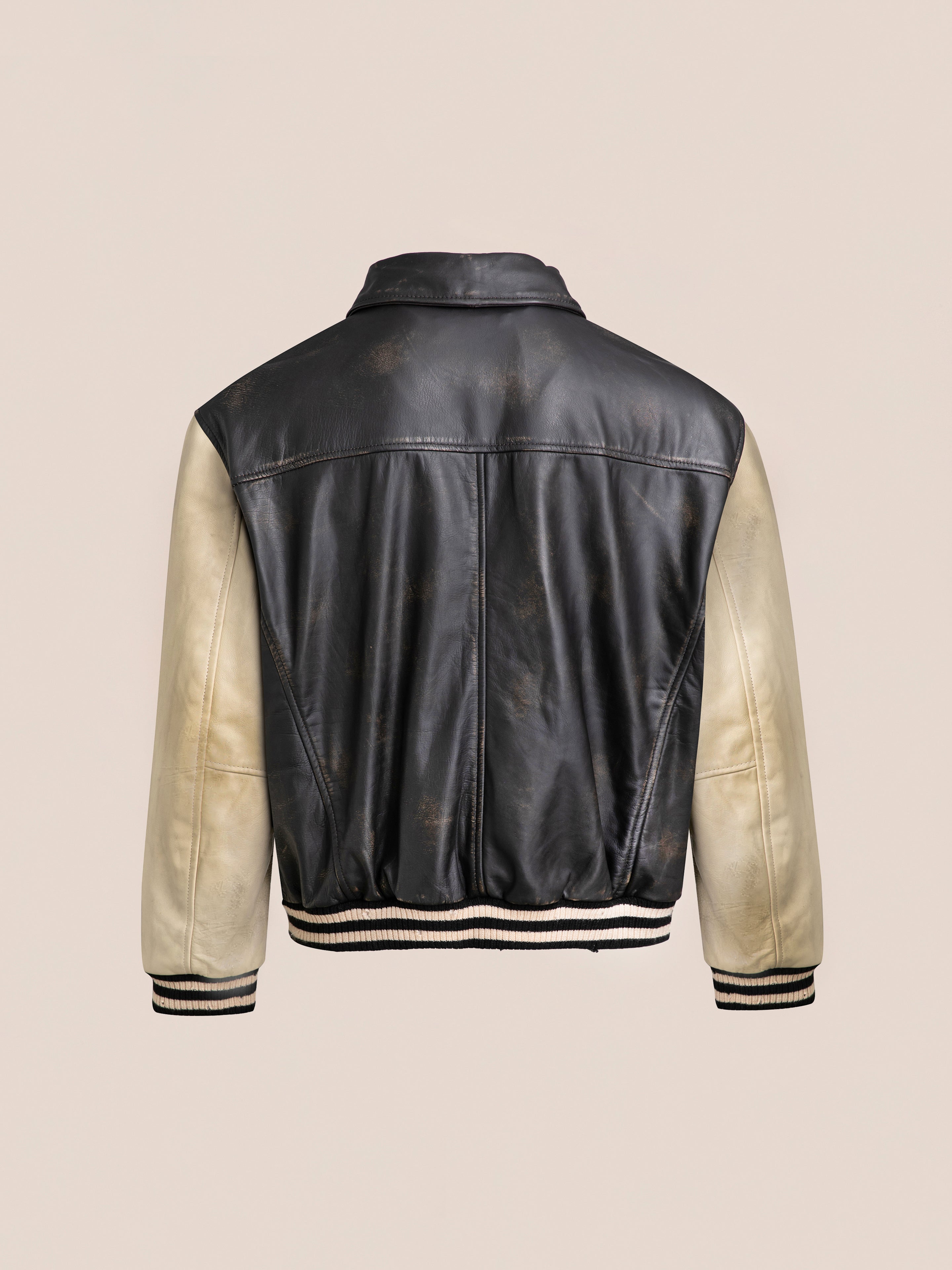 Back view of the FOUND Logan Distressed Leather Varsity Jacket in black and white leather with a striped hem and cuffs on a neutral background, featuring genuine hand-distressed leather and a smooth satin lining.