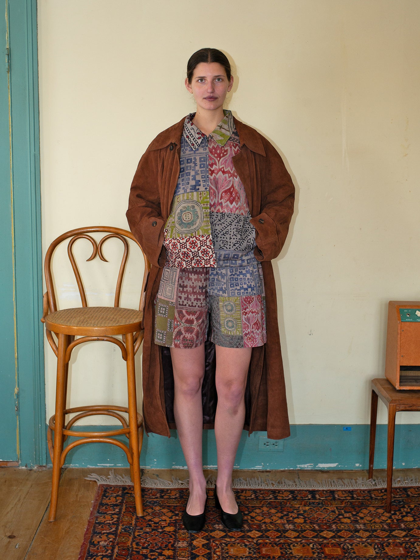 In a room, someone dons FOUND's Watercolor Mosaic Work Shorts with vintage patterns, standing beside a wooden chair on a decorative rug, embodying an effortless yet polished unisex relaxed fit.