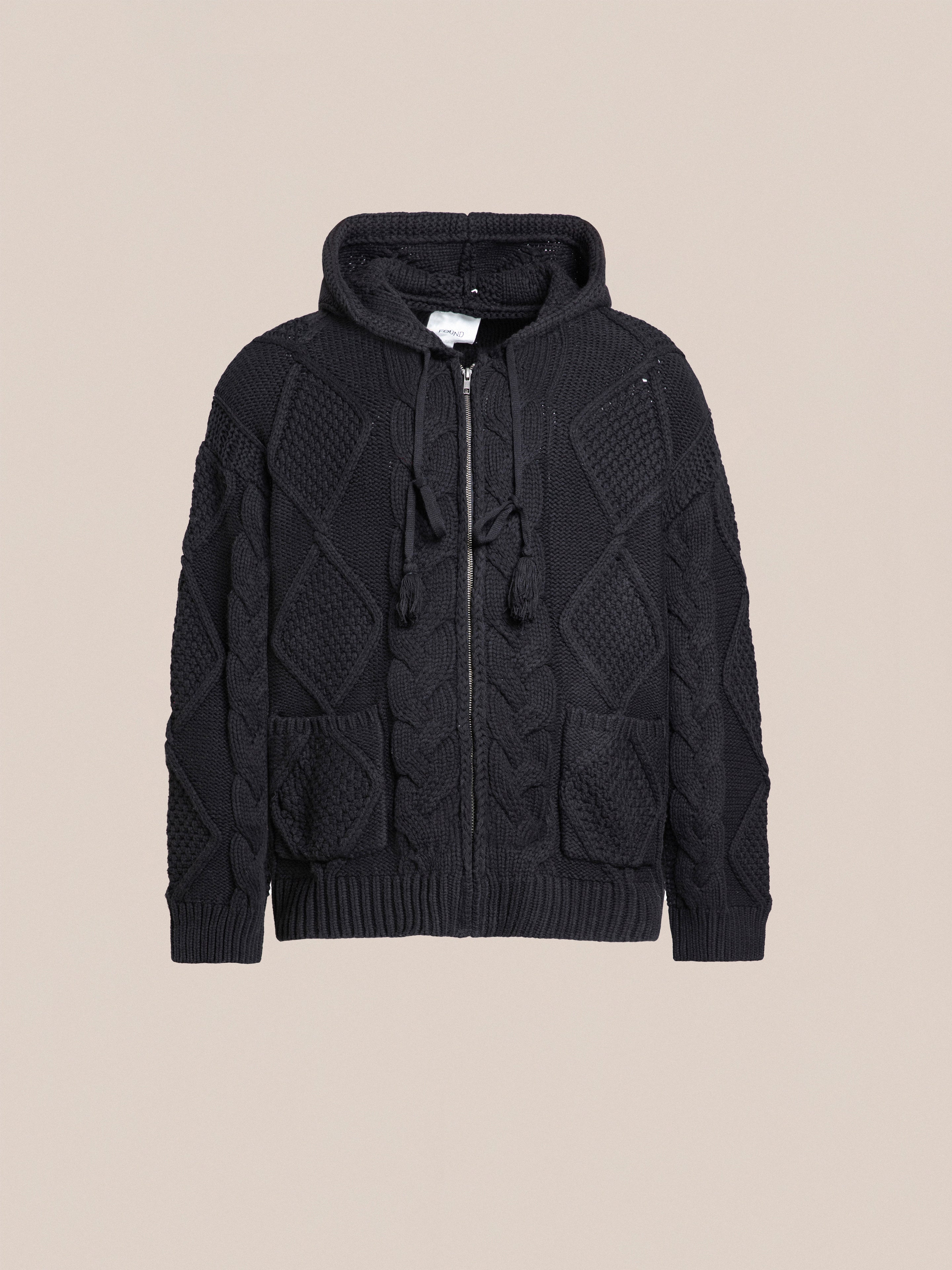 A black, chunky Found Zip Up Cable Knit Hoodie with a hood and drawstrings, featuring a textured diamond and cable-knit pattern on the front and sleeves for added comfort and warmth.