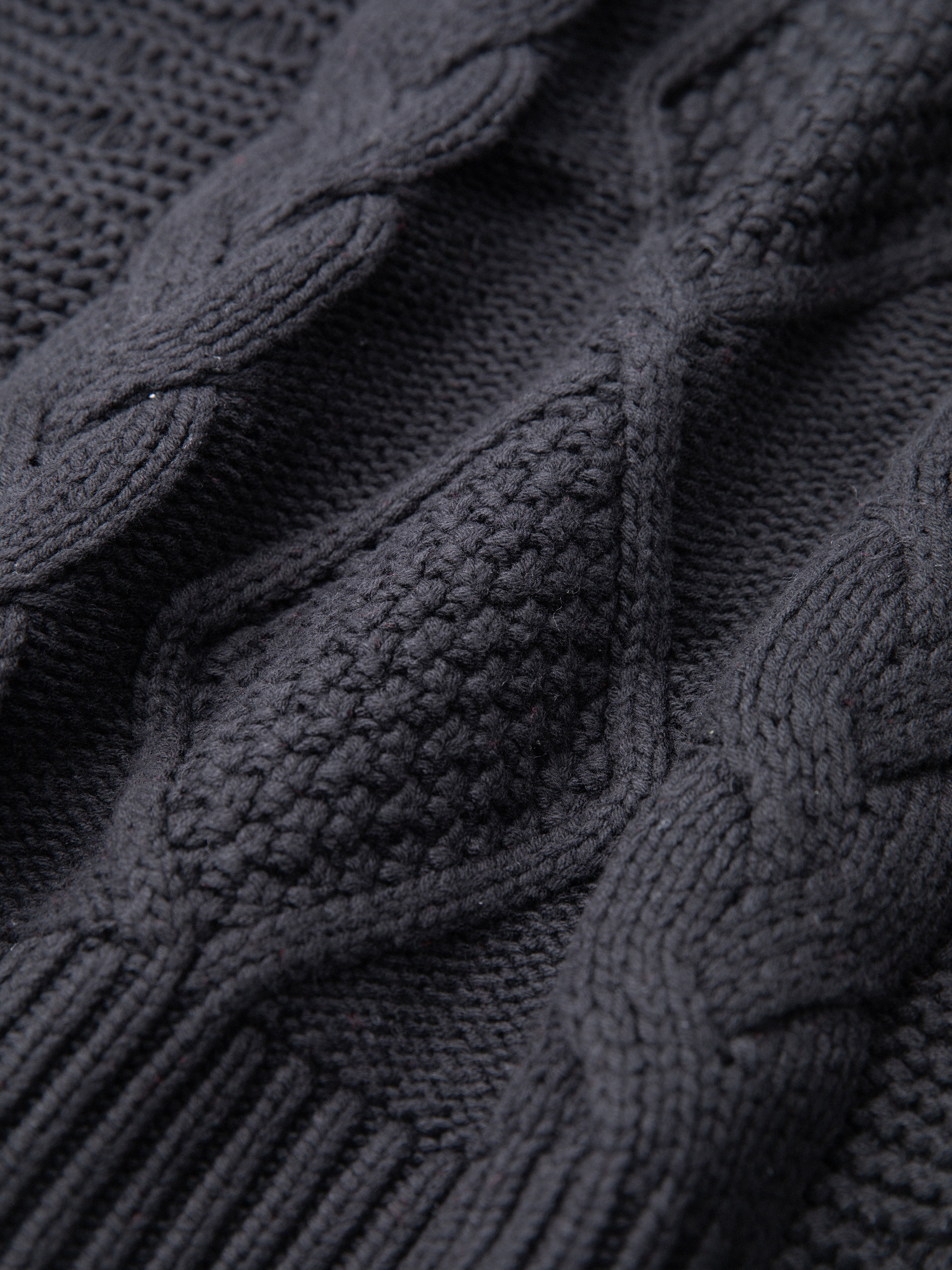 Close-up of a chunky knit black fabric featuring cable knit patterns interwoven with textured stitching, showcasing the comfort and warmth of a cozy Found Zip Up Cable Knit Hoodie.