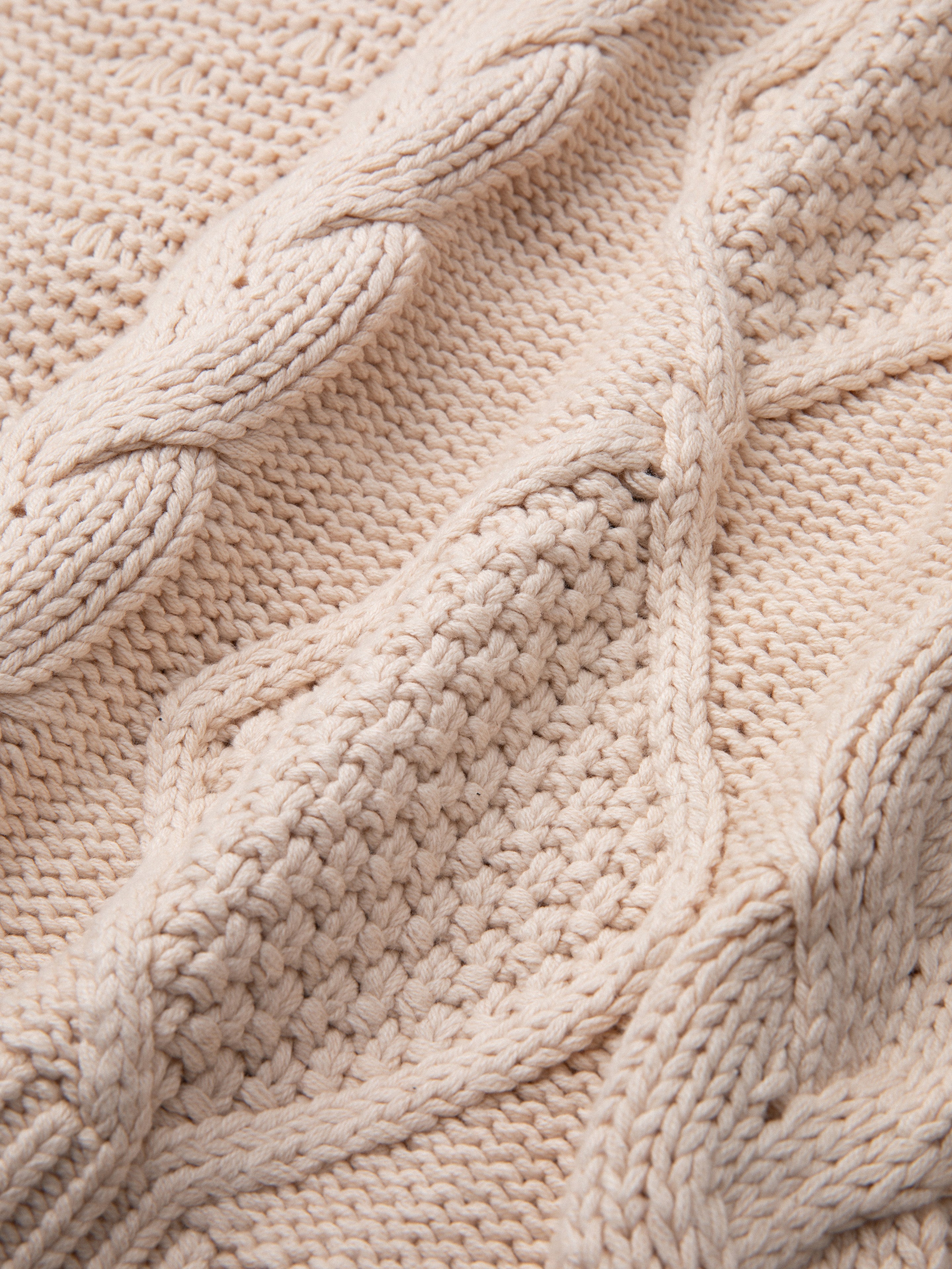 Close-up of a Found Zip Up Cable Knit Hoodie in beige with intricate patterns, including cable and textured stitches, evoking comfort and warmth.