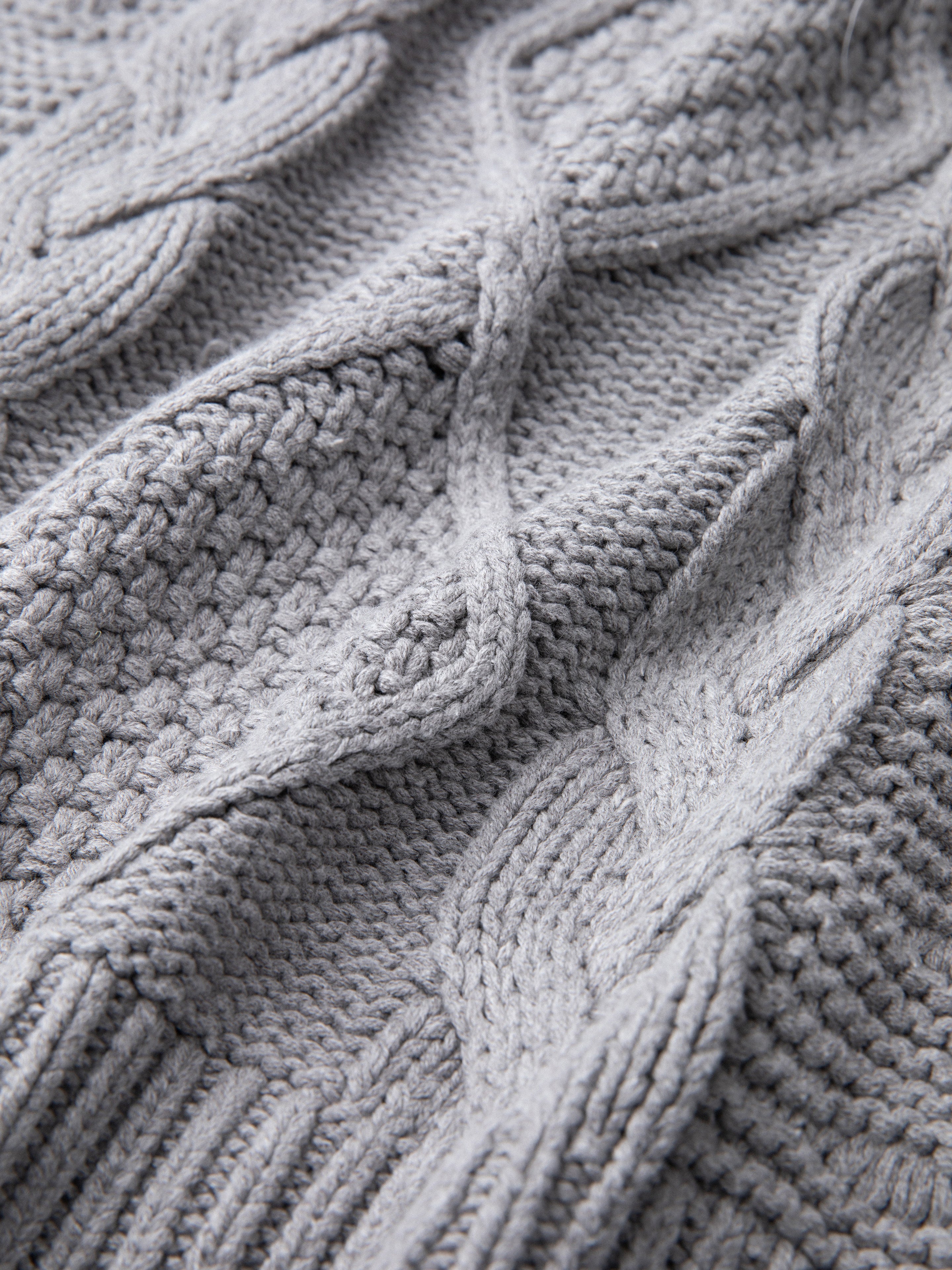 Close-up view of a grey chunky knit cable sweater showcasing its intricate pattern and texture, offering both comfort and warmth.