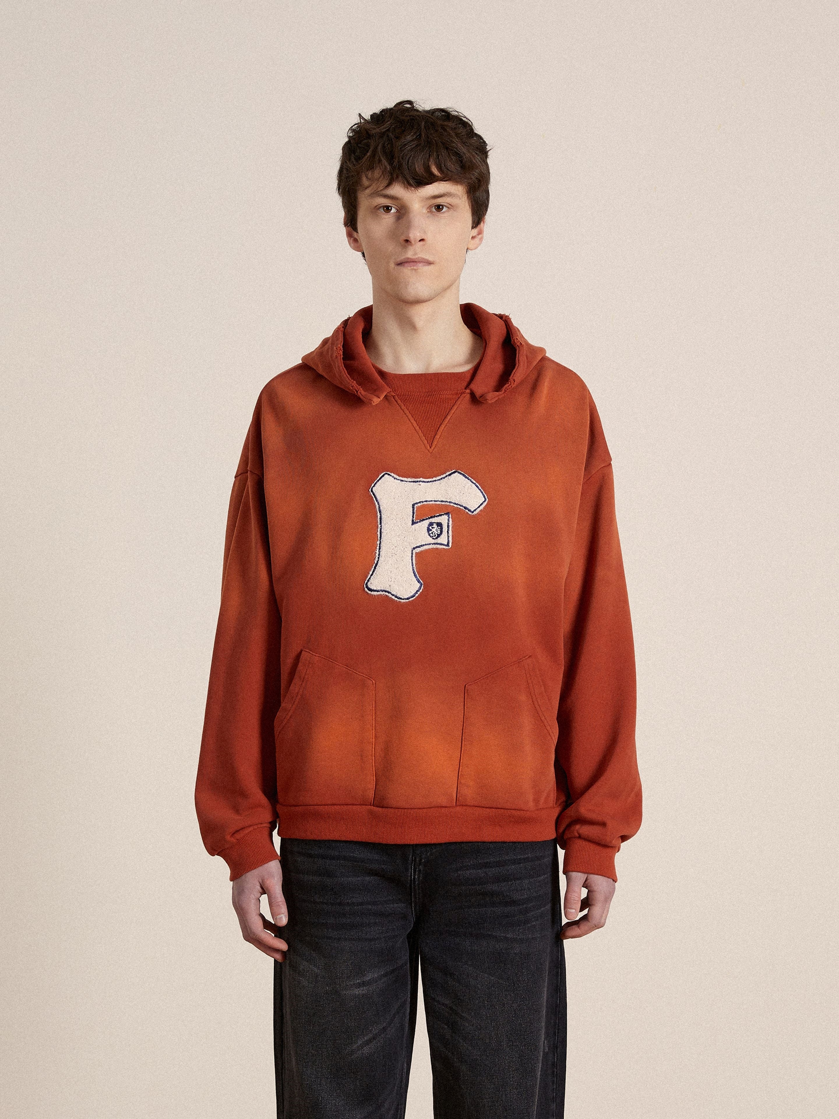 A man wearing an orange, enzyme washed cotton Faded "F" Hoodie with a faded "F" on it by Found.