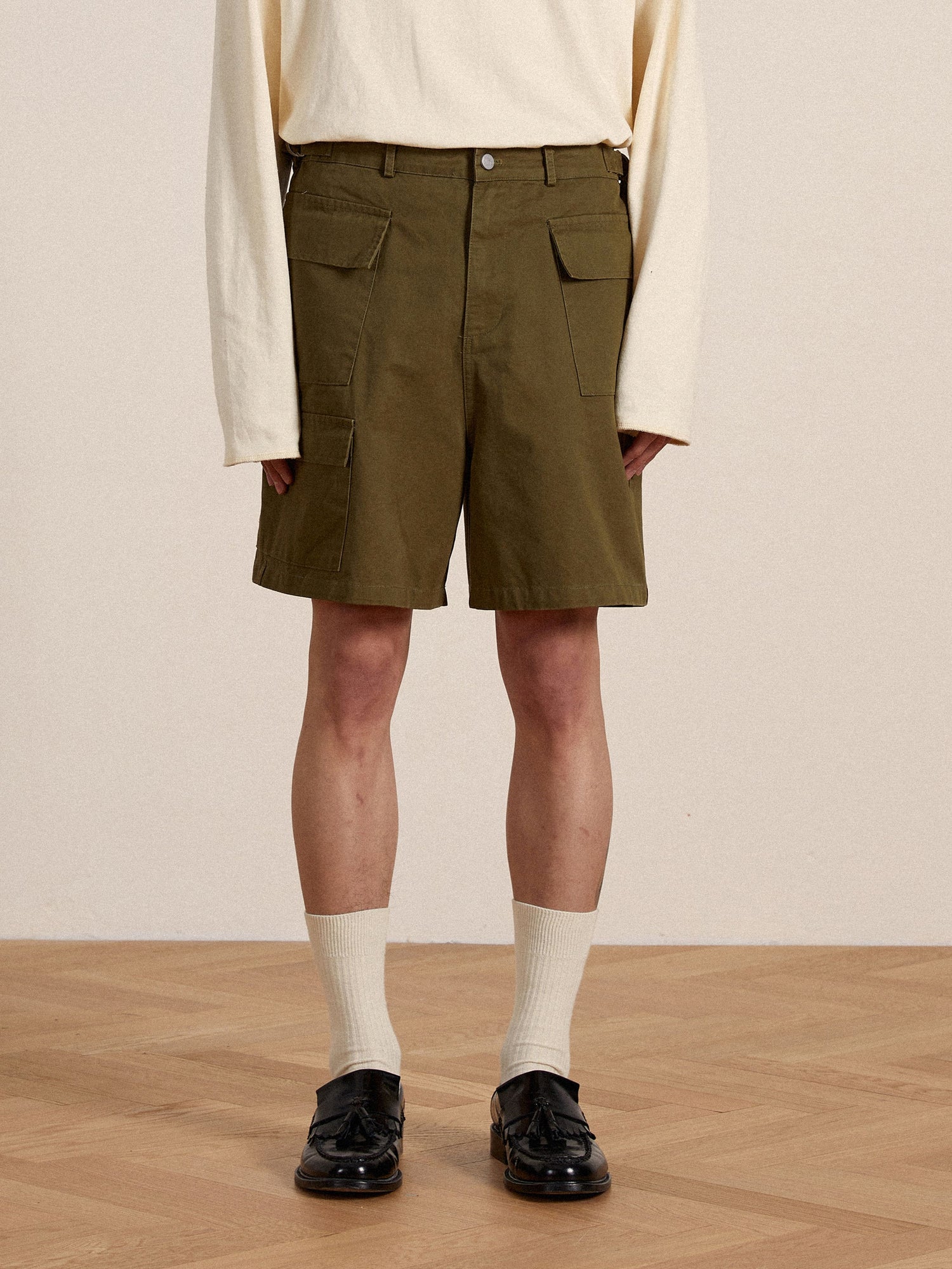 A man wearing green Found Twill Cargo Shorts with cargo pockets and a white shirt.