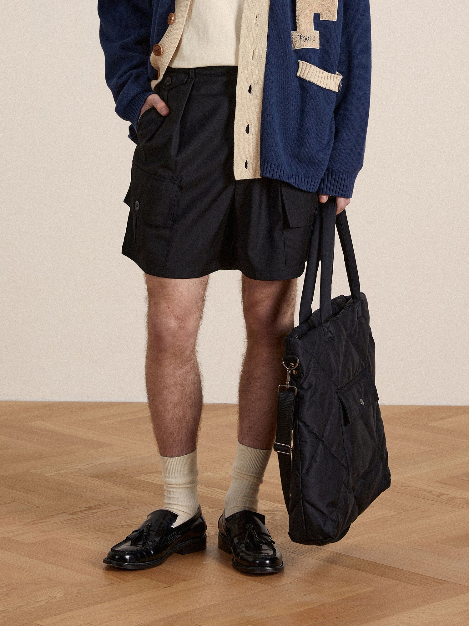 A man in Found Pleated Pocket Cargo Shorts and a sweater holding a bag.